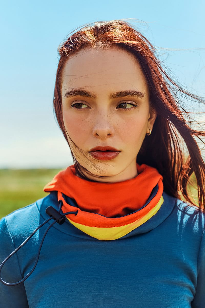 Close-up of a woman wearing a blue Merino Twiggy pullover with a red merino hoodie.