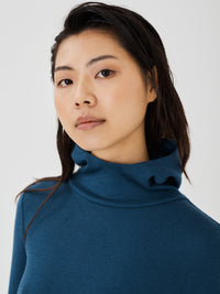 Zoomed-in front view of a women's blue merino wool hoodie by Šumska, featuring a high and wide neck design with soft, premium fabric texture.