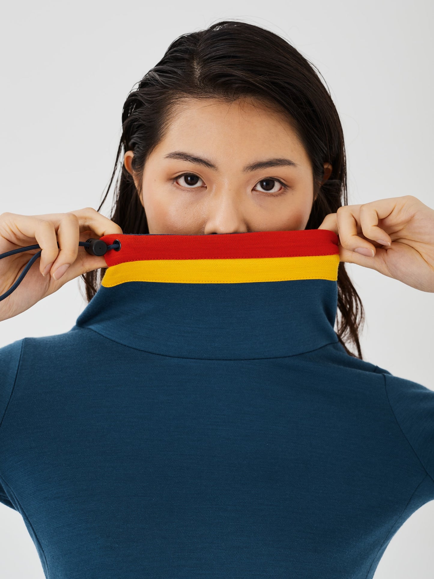 Zoomed-in close-up of a woman holding the collar of a blue merino wool Twiggy pullover jumper by Šumska, featuring vibrant red and yellow stripe panels."