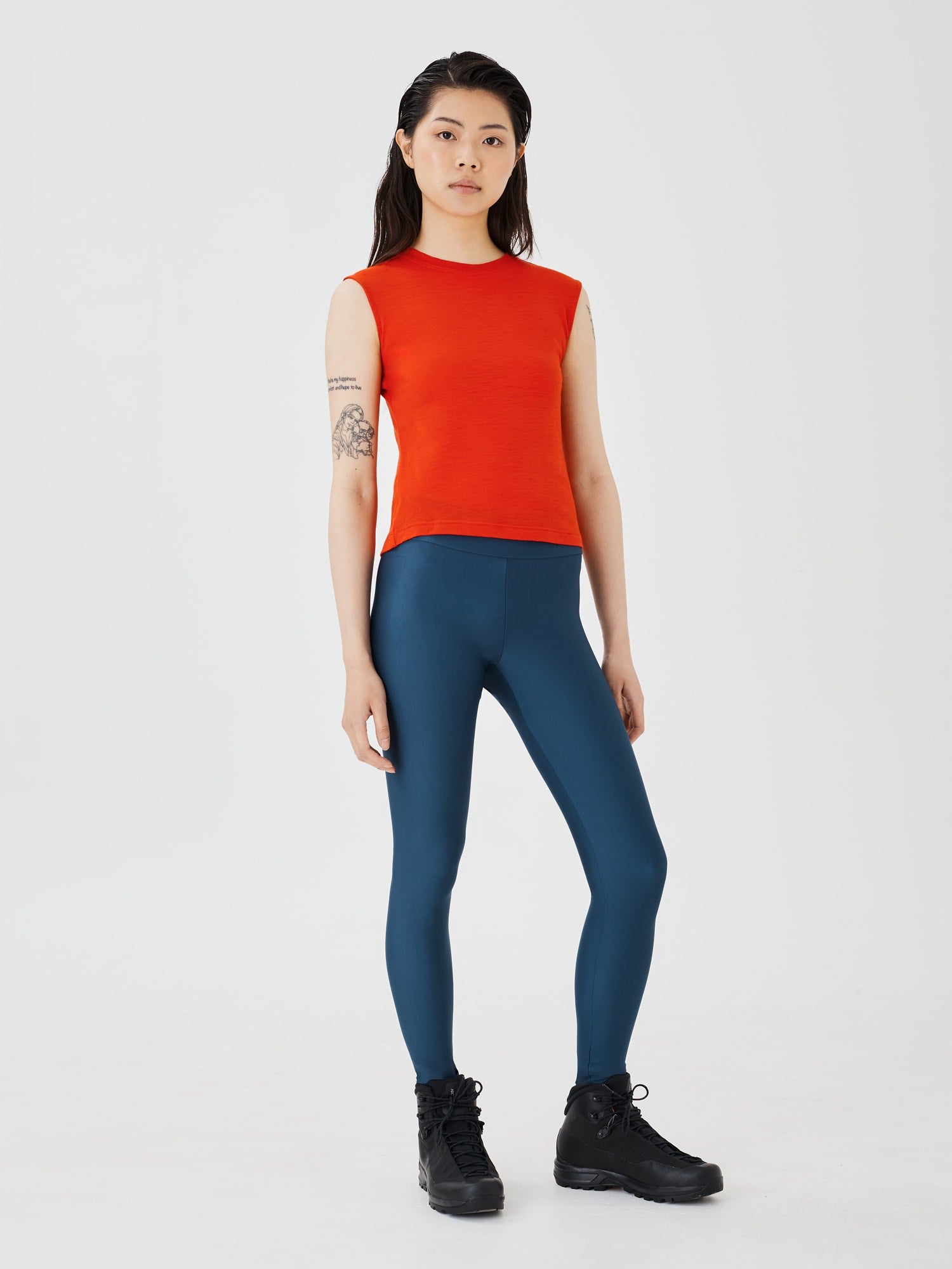 Full front view of a woman wearing blue performance leggings by Šumska, paired with a red merino sleeveless T-shirt, showcasing a sleek and athletic fit.