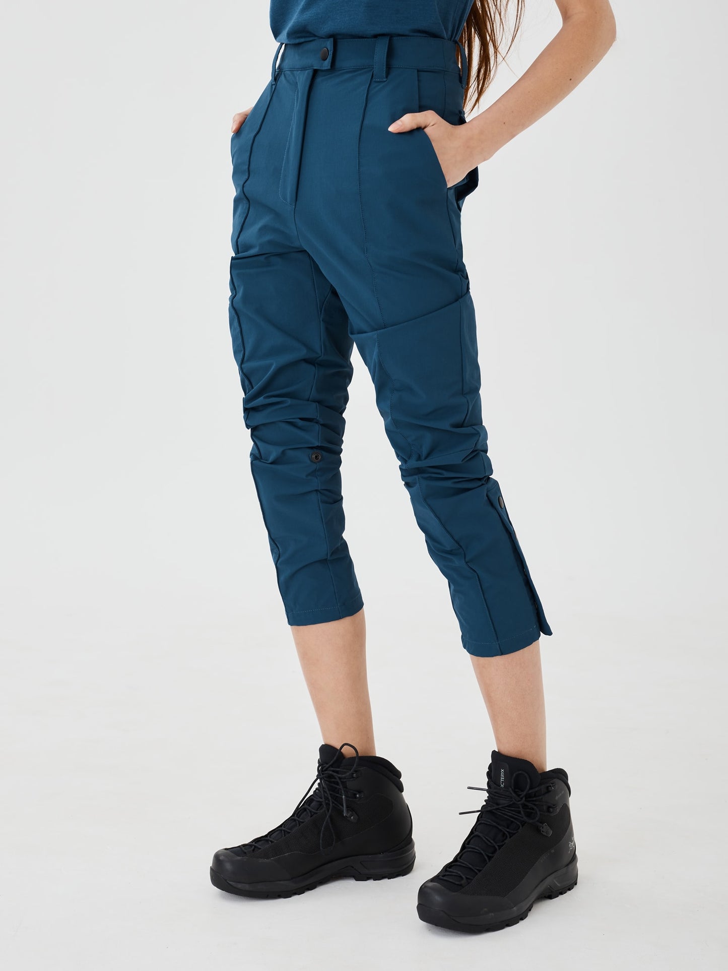 Blue Softshell Hiking Pants by Šumska worn at 3/4 length, with a woman standing with hands in pockets, highlighting the versatile fit and adjustable style