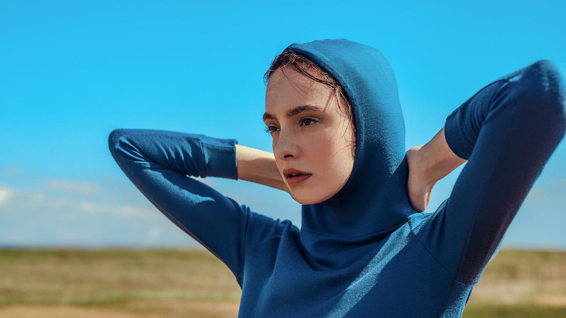 Woman wearing blue merino hoodie with hood on head.