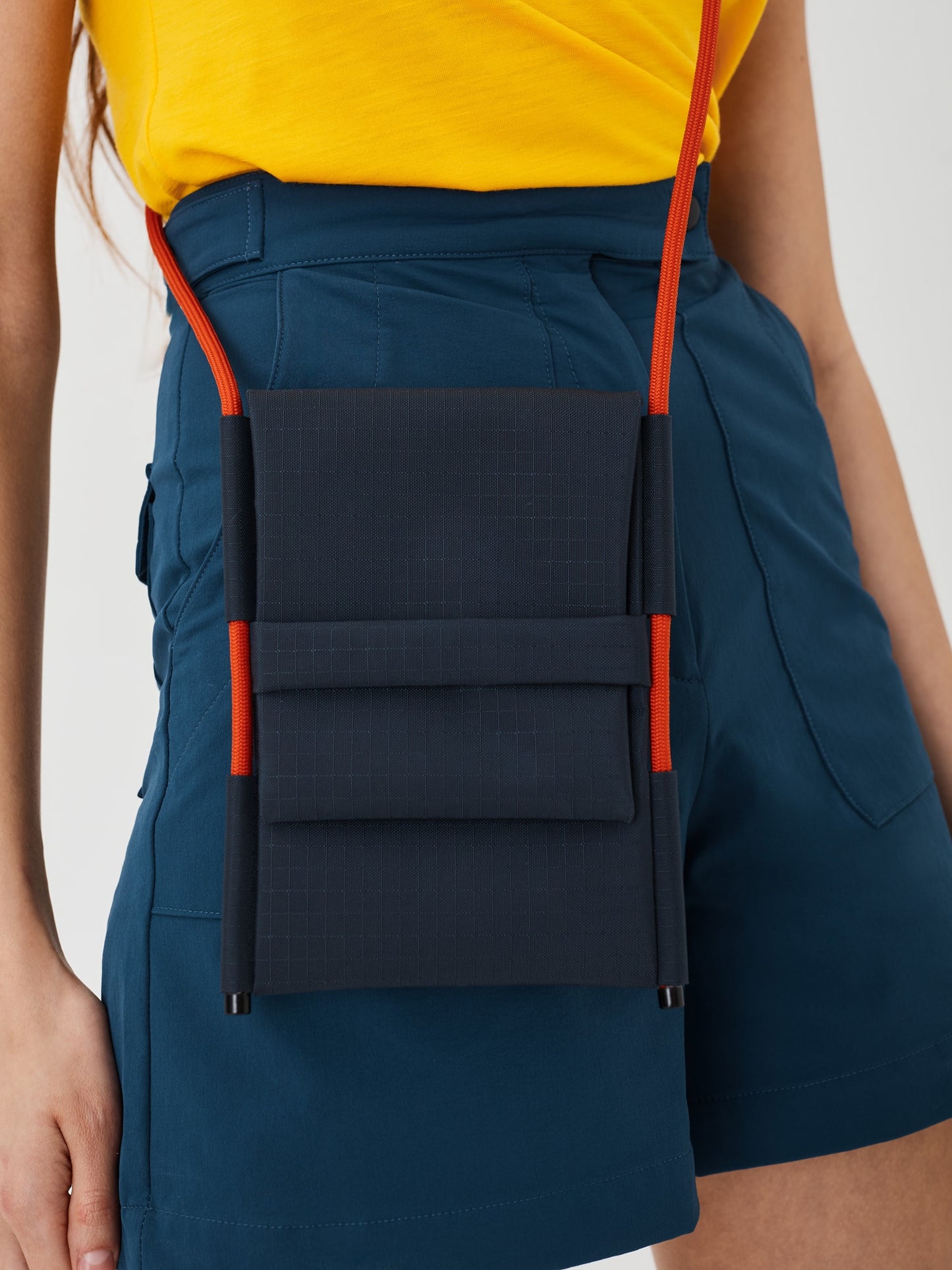 Zoomed-in view of a woman wearing the Šumska Cordura Crossbody iPhone Bag, displaying details like the solar orange Paracord rope strap, durable Cordura fabric, and compact design.