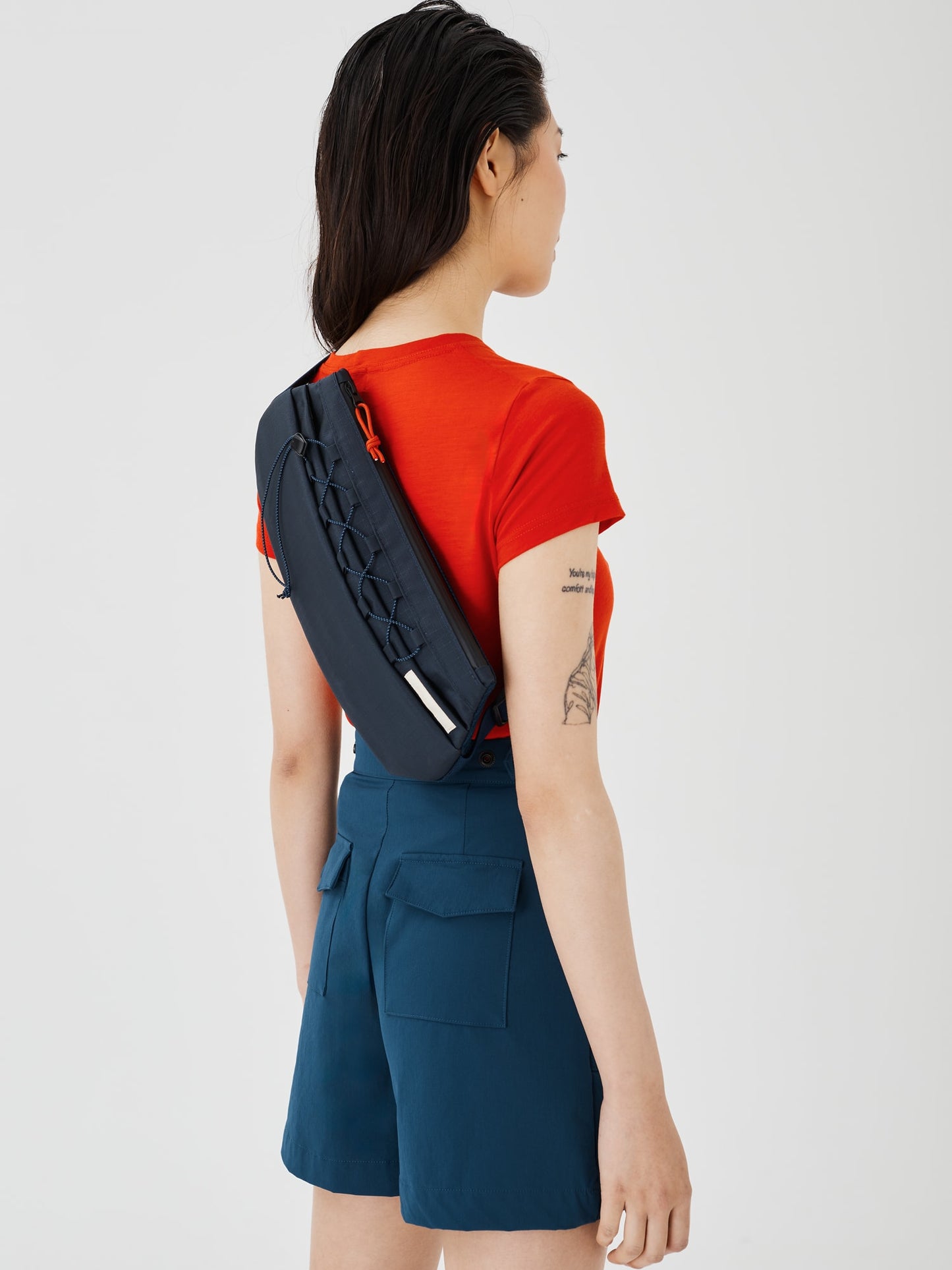 Zoomed-out view of the Šumska midnight blue Cordura sling bag worn on a woman's back, showing the overall design, adjustable strap, and ergonomic fit.