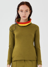 Close-up front view of an olive green merino wool Twiggy pullover jumper by Šumska, featuring a wide collar with vibrant red and yellow stripe panels, paired with olive green hiking pants.