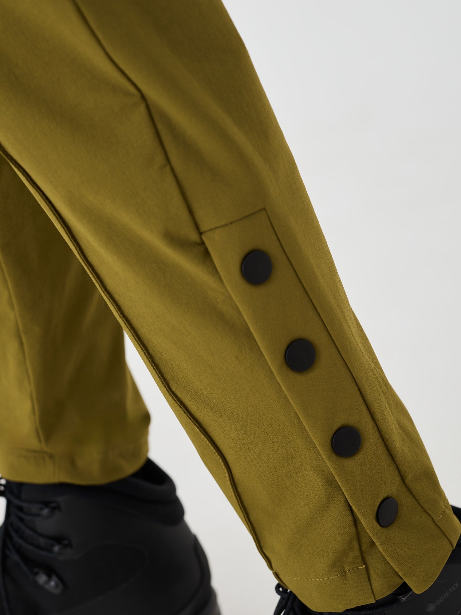 Close-up view of the ankle gusset on olive green Softshell Hiking Pants by Šumska, highlighting the black snap button features and versatile design.