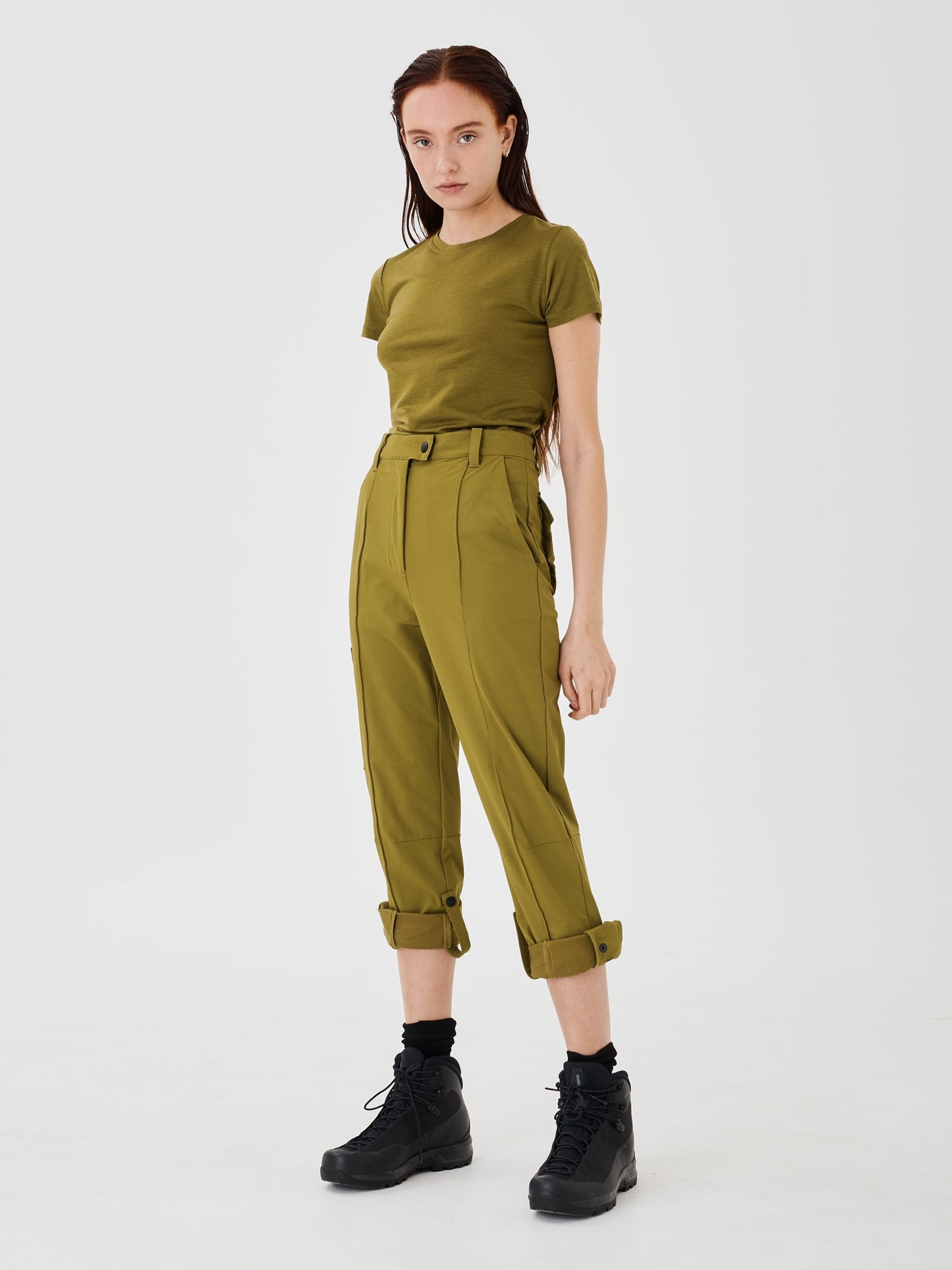 Olive green Softshell Hiking Pants by Šumska, rolled up to 3/4 length and secured with ties and snap buttons, paired with an olive green merino classic T-shirt, highlighting the adjustable design for versatile outdoor wear.