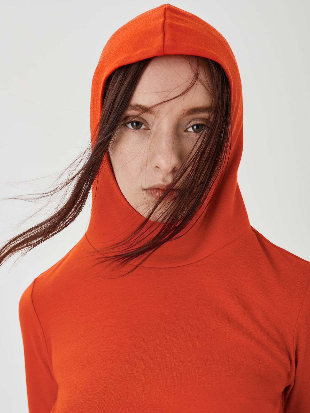 Close-up front view of a women's red merino wool hoodie by Šumska, with the hood on, highlighting the clean, minimal design and premium fabric texture. 
