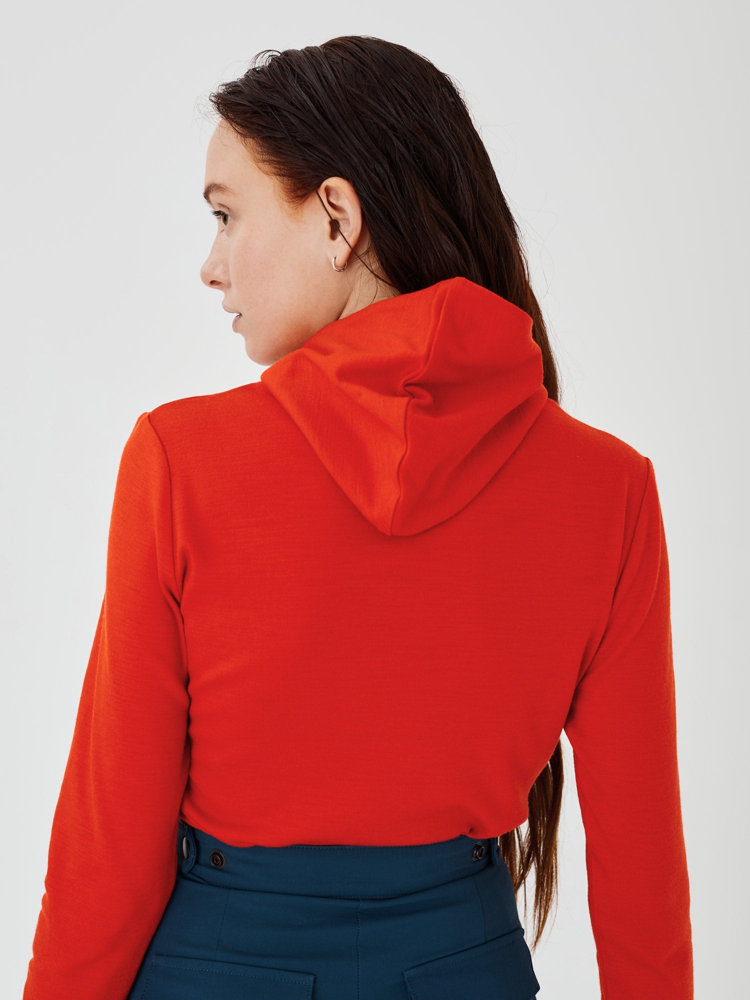 Back view of a women's red merino wool hoodie by Šumska, showcasing the hood design and slim, comfortable fit.