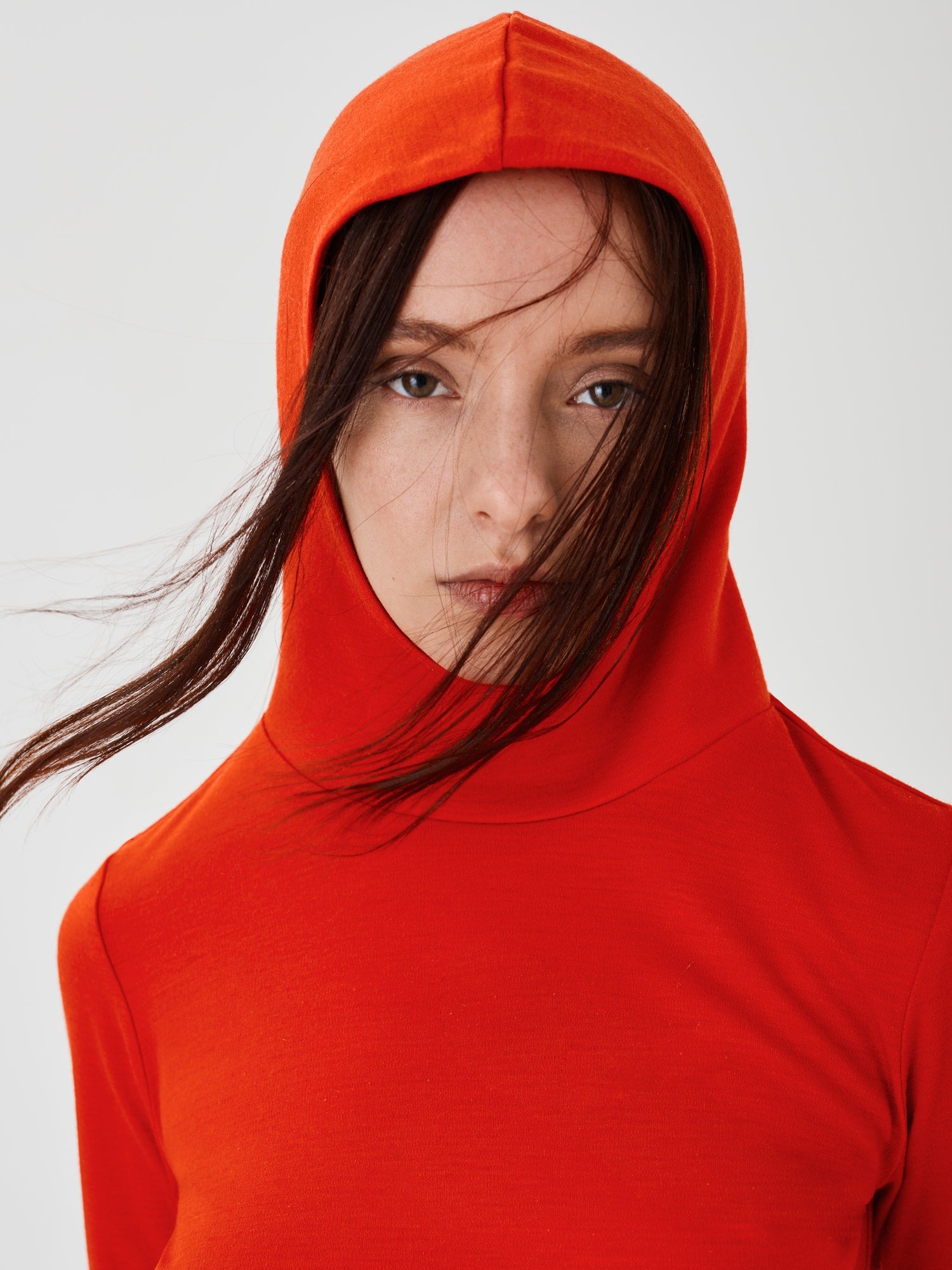 Close-up front view of a women's red merino wool hoodie by Šumska, with the hood on, highlighting the clean, minimal design and premium fabric texture.