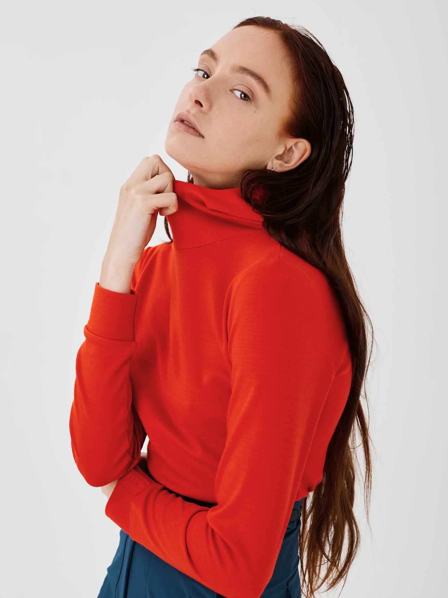 Front close side view of a women's red merino wool hoodie by Šumska, highlighting the high, wide neck design and the clean, minimal style with cozy fabric texture.