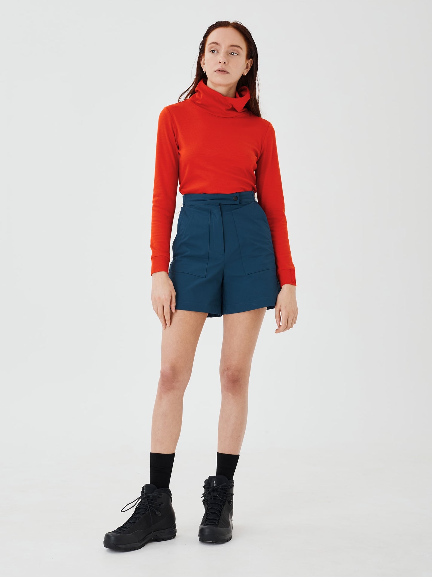 Full front view of a women's red merino wool hoodie by Šumska, paired with blue shorts, highlighting the clean, minimal design and cozy fit.