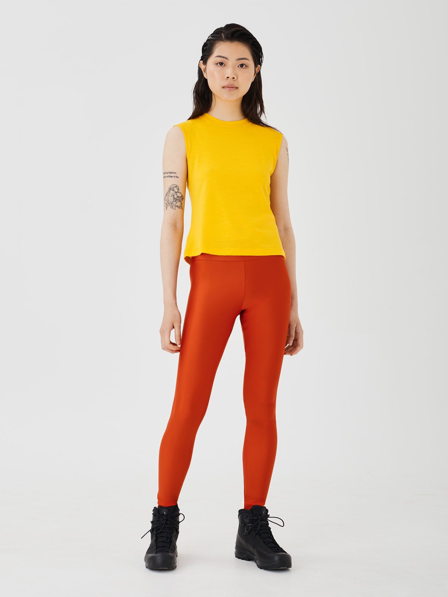 Full front view of a woman wearing rust-coloured performance leggings by Šumska, paired with a yellow merino sleeveless T-shirt, highlighting the sleek design and comfortable fit.