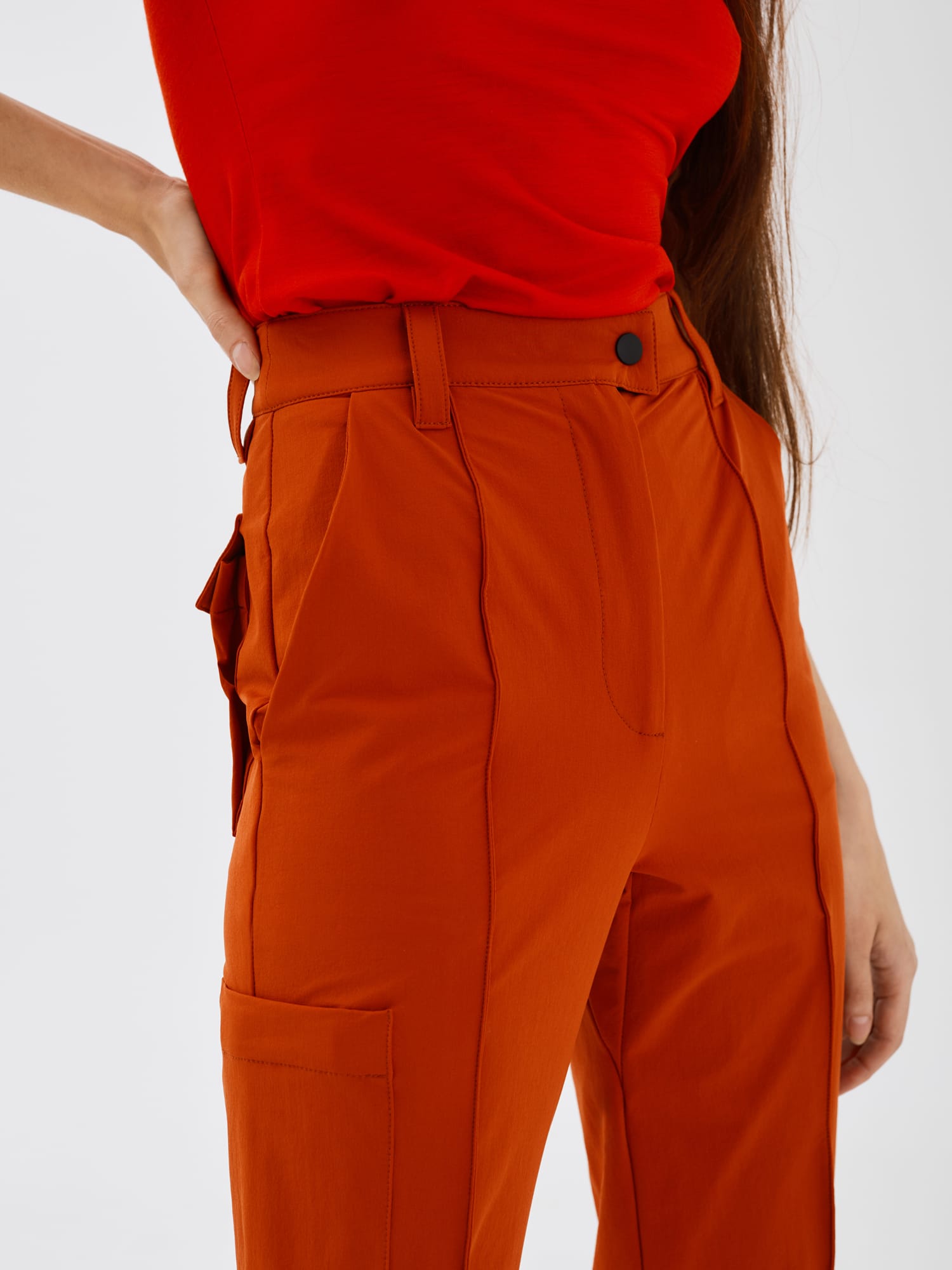 Close-up side view of rust-coloured Softshell Hiking Pants by Šumska, displaying front, side, and back pockets with detailed stitching.