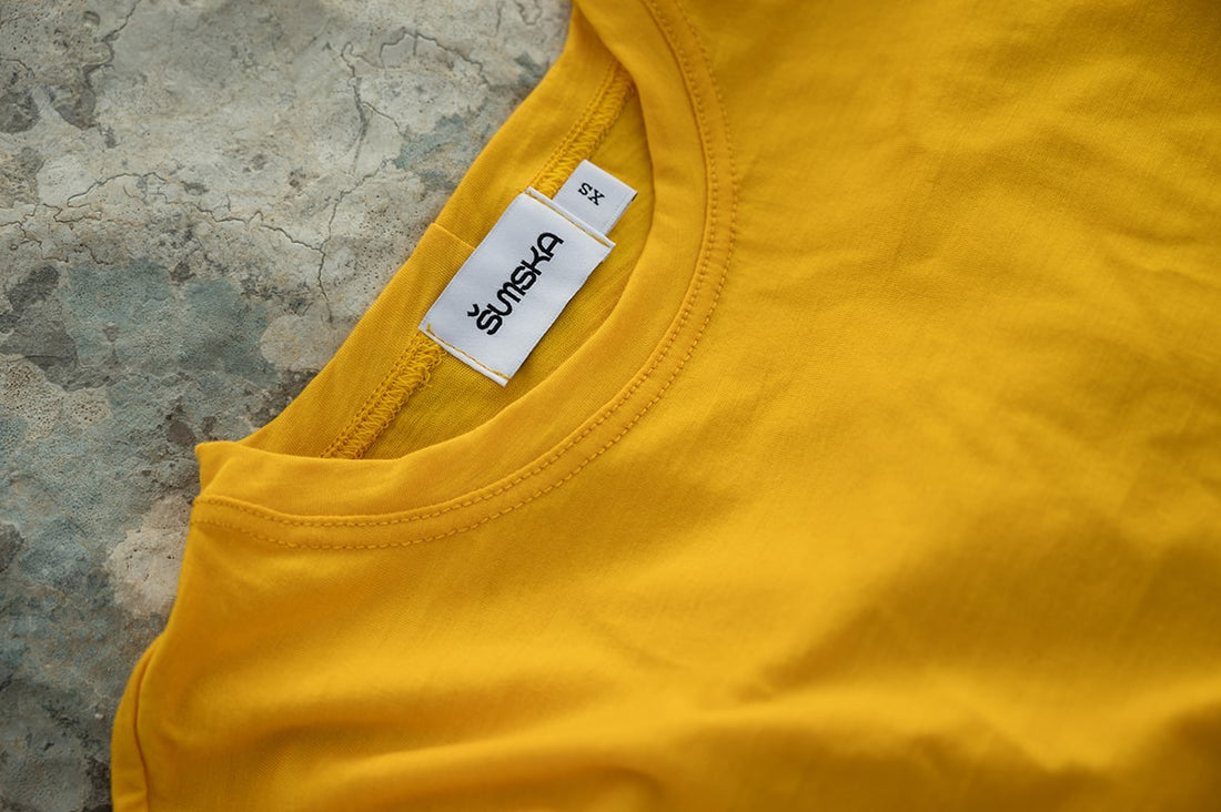 Yellow Merino Wool Classic T-Shirt by Šumska on a rock, highlighting its vibrant colour and minimalist design.