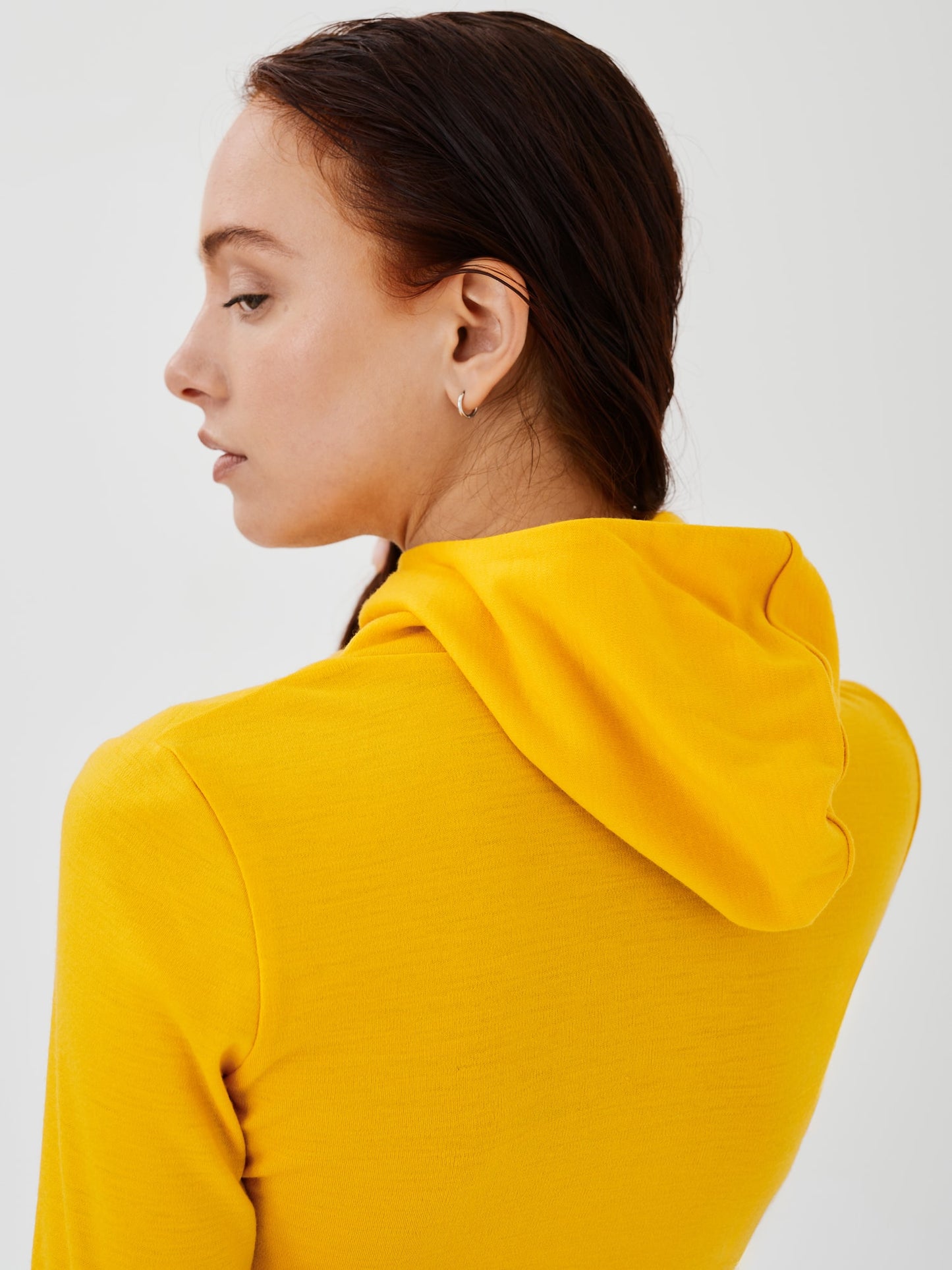 Back view of a women's yellow merino wool hoodie by Šumska, showcasing the hood design and slim, comfortable fit.