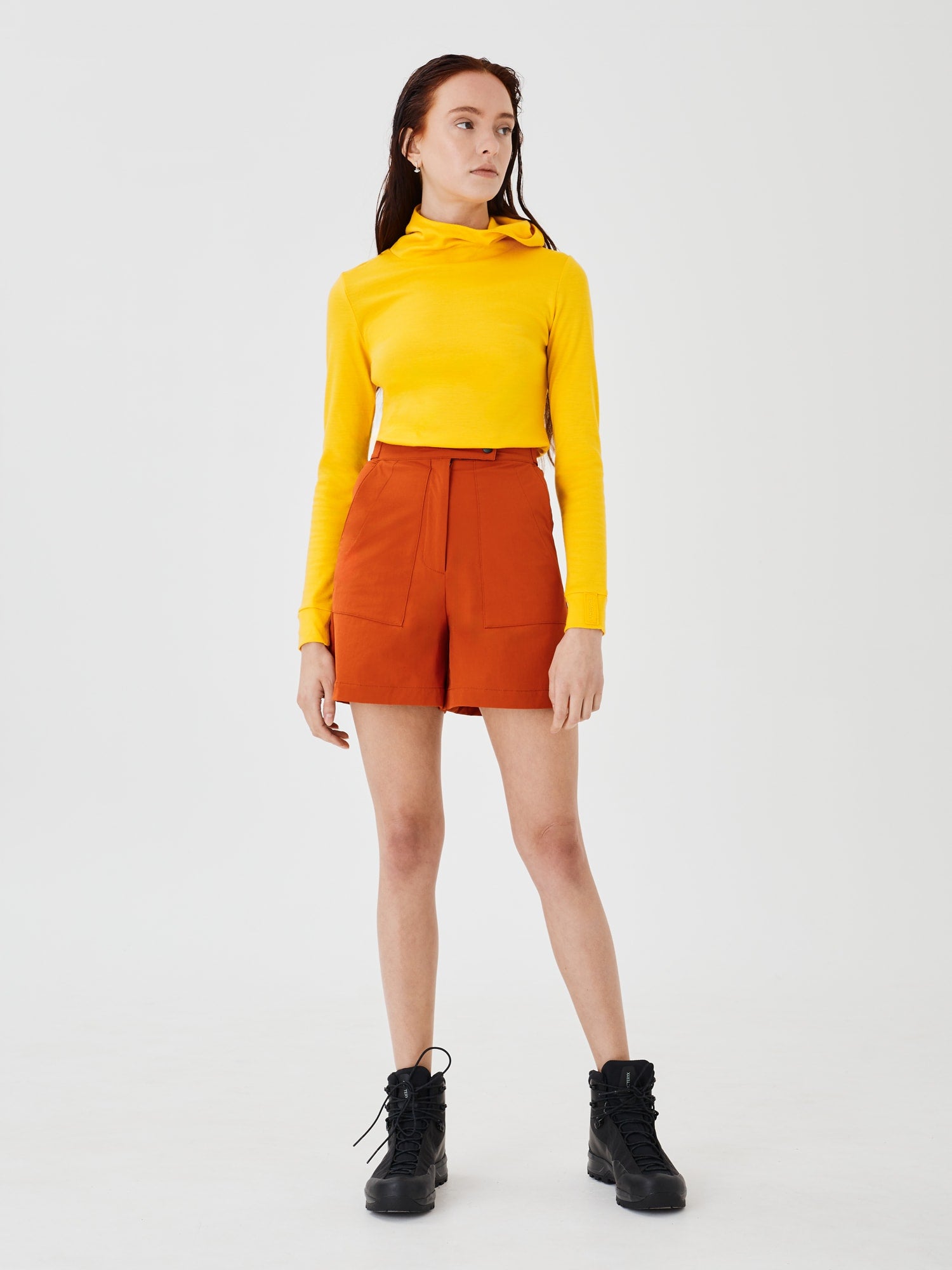 Full front view of a women's yellow merino wool hoodie by Šumska, paired with rust shorts, highlighting the clean, minimal design and comfortable fit.